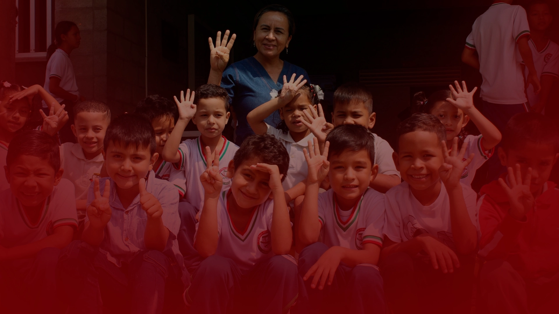Grupo de niños de colegio haciendo el gesto con las manos del número 4, acompañados de una profesora que también hace el mismo gesto, todos participando en el proyecto 'Los de la 4 para la U'
