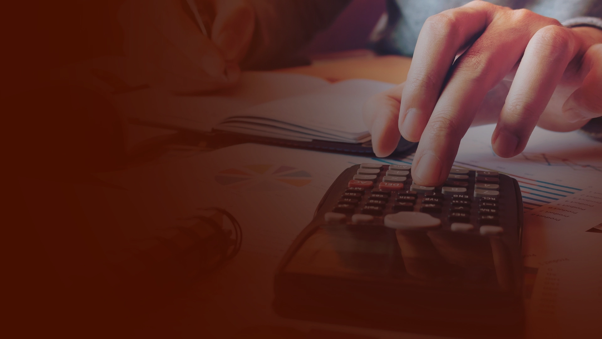 Calculadora y manos realizando cálculos de estados financieros, con papeles y gráficos en el fondo.